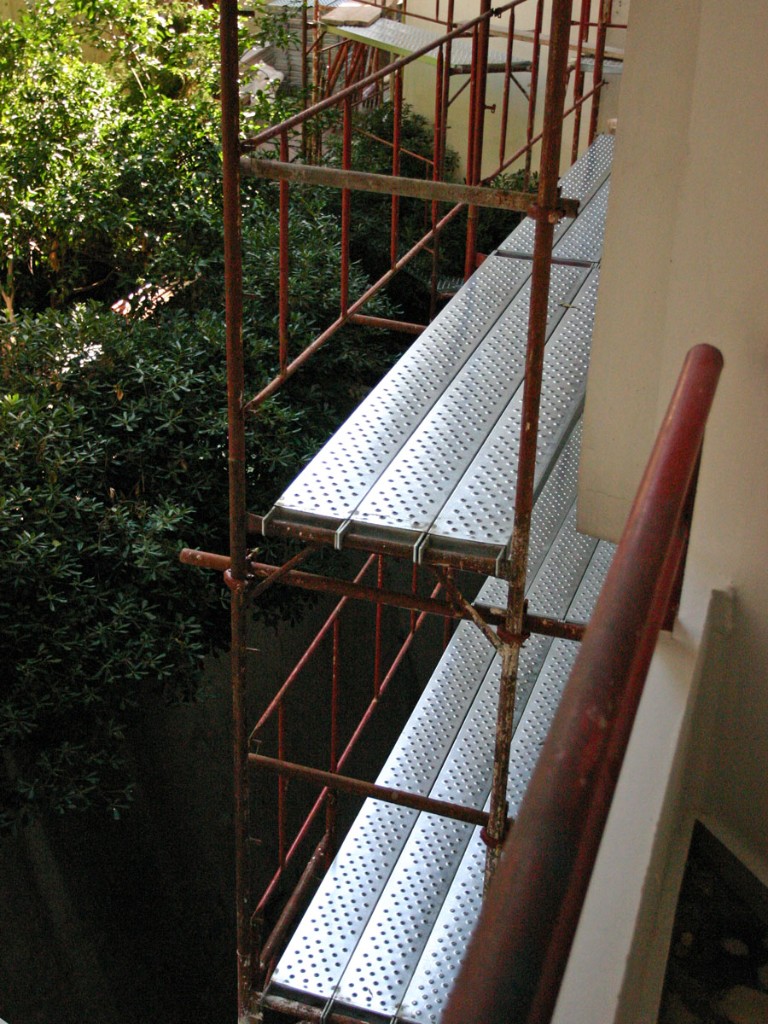 Λεπτομέρεια κατακόρυφης σκαλωσιάς με καταστρώματα και πράσινο περιβάλλον.